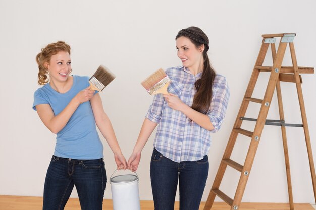 Friends holding paint brushes and can in a new house