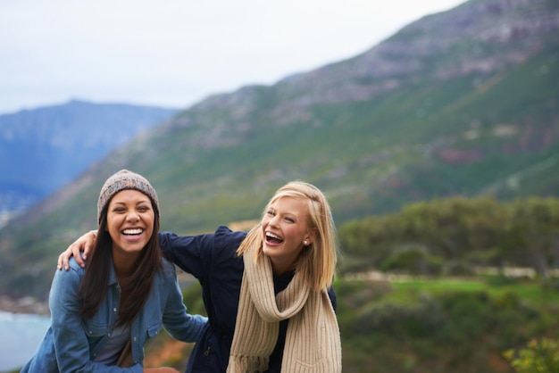 Photo friends laugh and women on mountain happy for adventure on holiday vacation and weekend outdoors nature travel and people by seaside for hike funny joke and bonding together in countryside