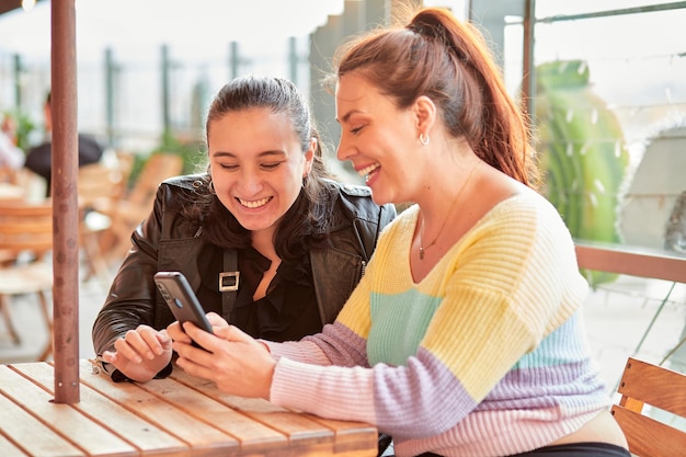 Photo friends laughing at outdoor restaurant looking at phone screen