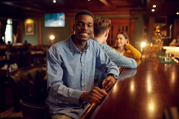 Friends leisures at the counter in bar, nightlife. Group of people relax in pub, night lifestyle, friendship, event celebration