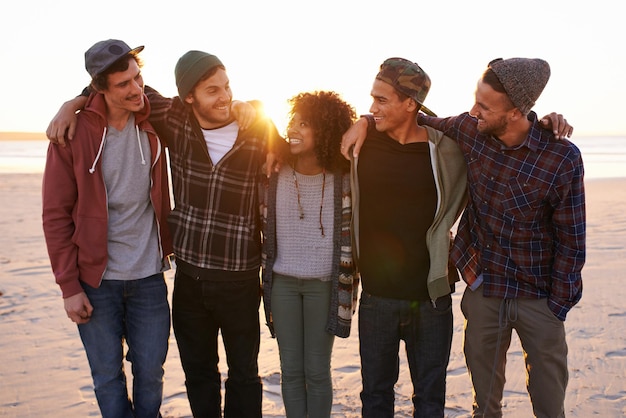 Photo friends make the world a better place shot of a group of friends walking along a beach at sunset