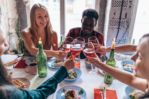 Friends making toast clinking glasses above dinner table