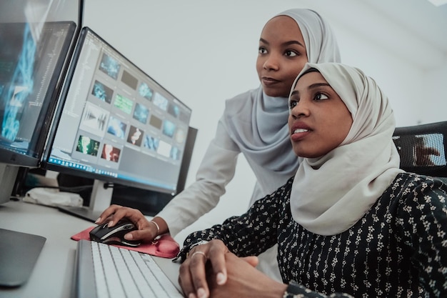 Friends at the office are two young Afro-American modern Muslim businesswomen wearing scarfs in a creative bright office workplace with a big screen. High-quality photo. High-quality photo