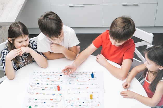 Photo friends play board game with dice and chips on table from above view kids look at boy throw dice and move figure