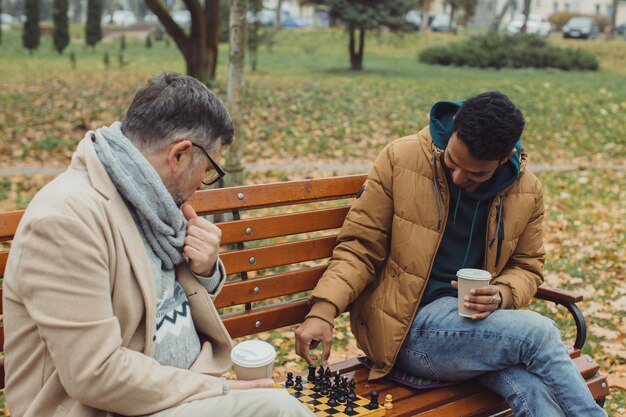 秋の公園のベンチでチェスをする友達 さまざまな年齢の人々の多文化的な友情