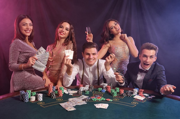 Friends playing poker at casino at table with stacks of chips money cards on it Celebrating win smiling Black smoke background Closeup