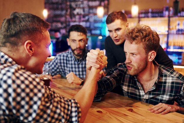 Friends plays arm wrestling Group of people together indoors in the pub have fun at weekend time