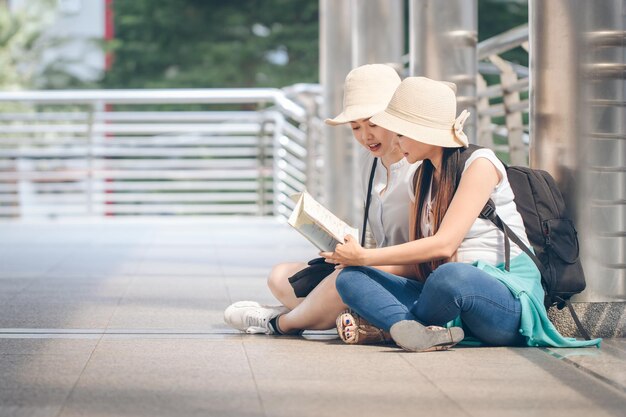 Friends reading book while sitting on bridge in city