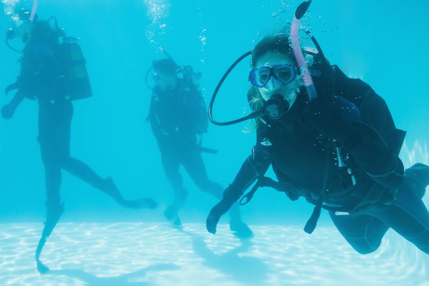 Gli amici sull'addestramento subacqueo sono immersi nella piscina uno che guarda alla macchina fotografica