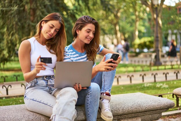 Friends shopping online with laptop and credit card in park