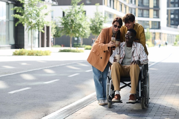 Friends showing photos on smartphone to their friend with disability during their walk outdoors