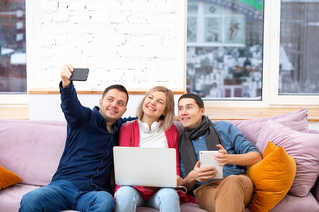 Friends sit on the couch chatting and using a smartphone desktop computer laptop