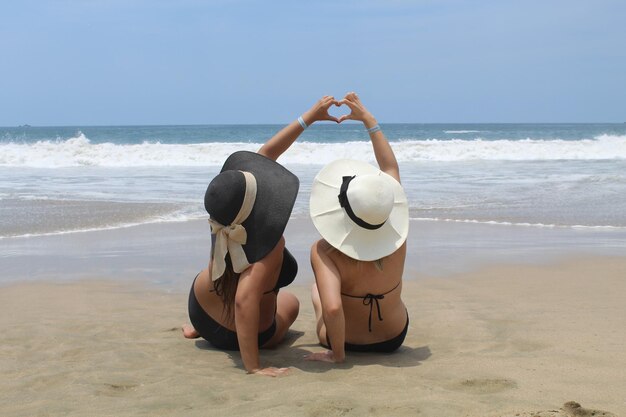 Photo friends sitting on beach against clear sky