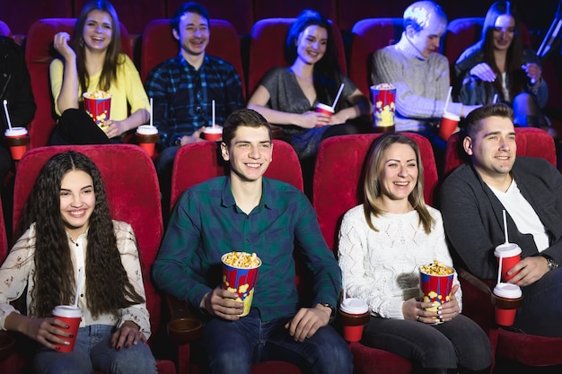 Friends sitting in a cinema watch film eating popcorn