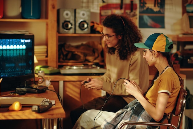 Friends sitting in front of tv monitor and playing video game together in garage during leisure time