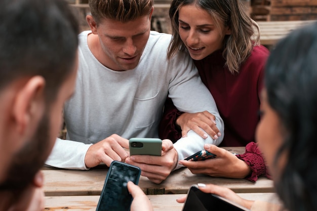 Photo friends sitting outdoors holding and using smartphones