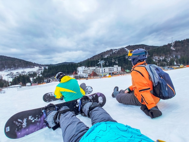 スノーボードで雪の丘に座っている友達。冬のアクティビティ。人物ビュー