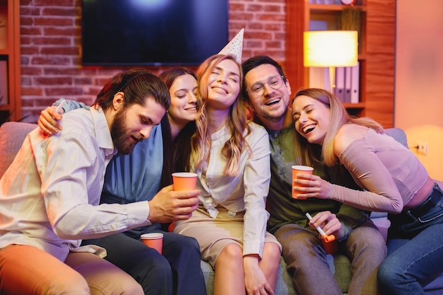 Friends sitting on a sofa in a cozy room and celebrating birthday