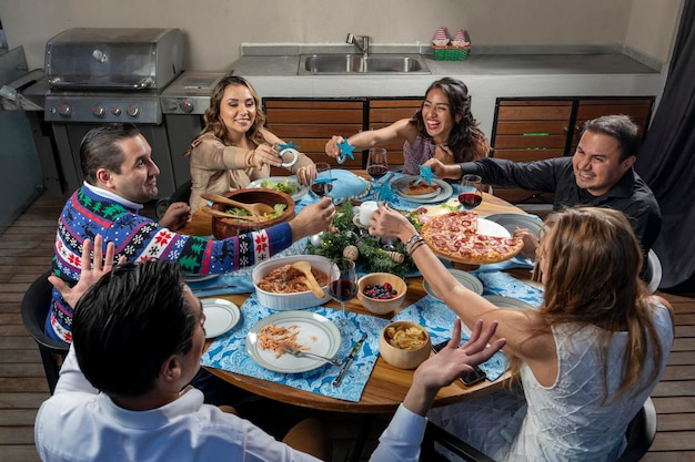 Amici che sorridono mentre vivono insieme a natale seduti a un tavolo che mostra l'arredamento natalizio