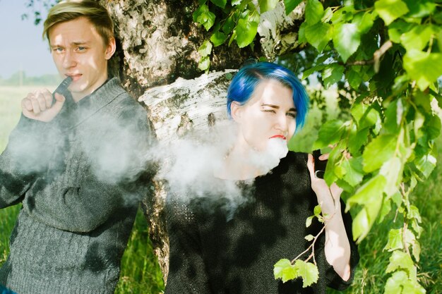 Photo friends smoking while standing by tree on field