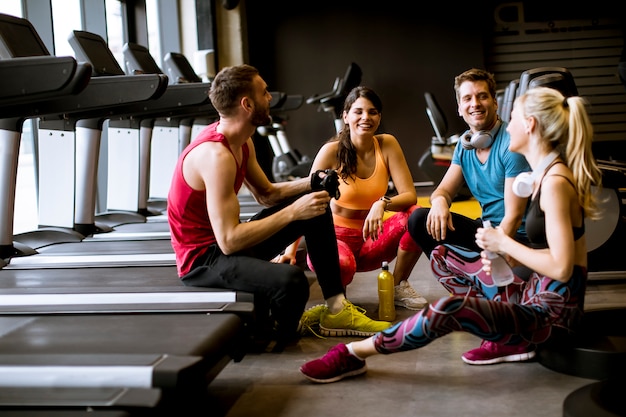 Amici in abiti sportivi a parlare e ridere insieme, seduti sul pavimento di una palestra dopo un allenamento