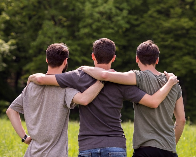 Friends standing on glade with hands on each other shoulders