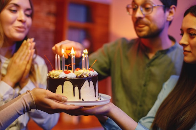 Photo friends standing together holding a plate with a cake and celebrating birthday