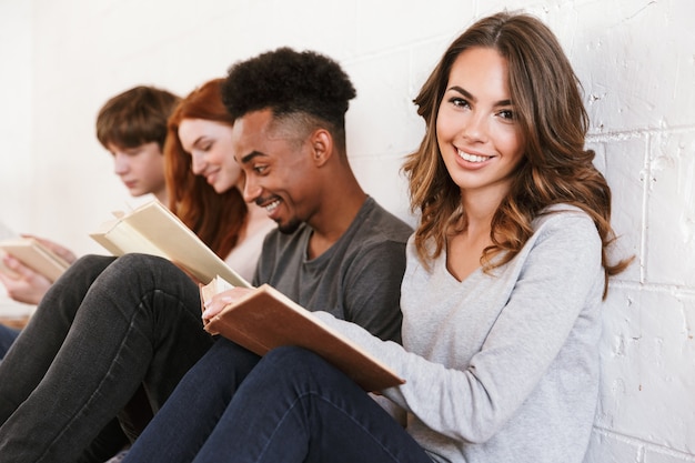 Foto studenti di amici che si siedono sopra il muro bianco. concentrarsi sulla donna allegra.