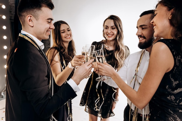 Friends in stylish elegant clothes smile together holding glasses of champagne in hands