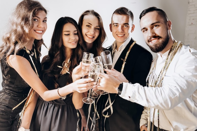 Friends in stylish elegant clothes smile together holding glasses of champagne in hands