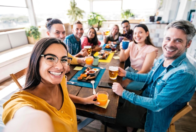 Amici che si fanno selfie al ristorante pub sul tetto - giovani che si divertono insieme alla brasserie all'ora del brunch - famiglia felice che ride e si diverte al bar caffetteria del saloon - filtro colore brillante e vivido