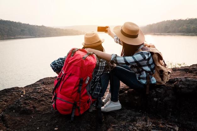 Friends taking selfie through mobile phone against lake during sunset