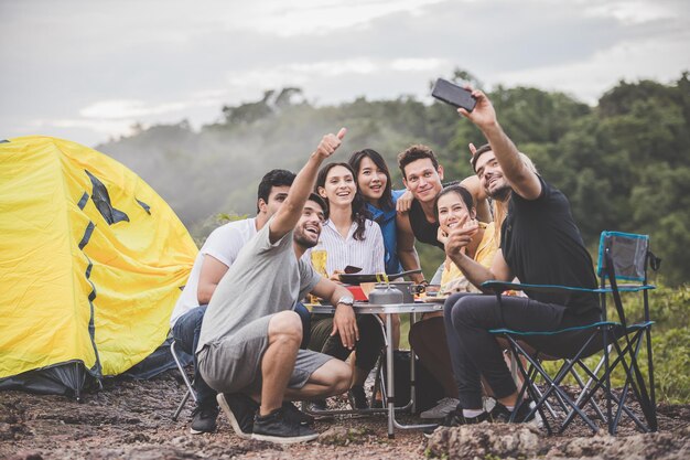 Photo friends taking selfie while sitting on land by tent against sky