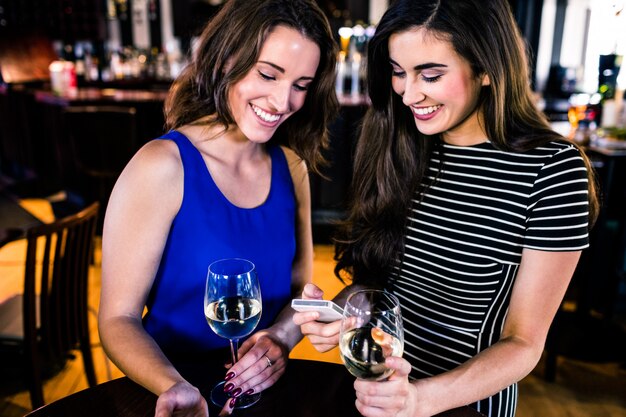 Friends texting and having a glass of wine in a bar