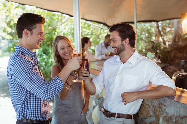 Friends toasting glass and bottle of alcohol at counter in restaurant