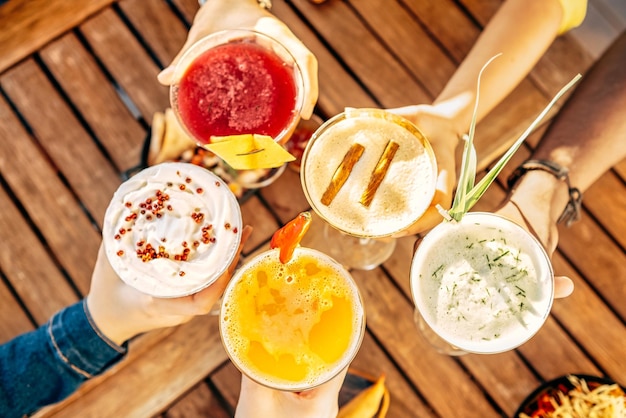 Friends toasting saying cheers holding tropical fruit cocktails Young people having fun at bar