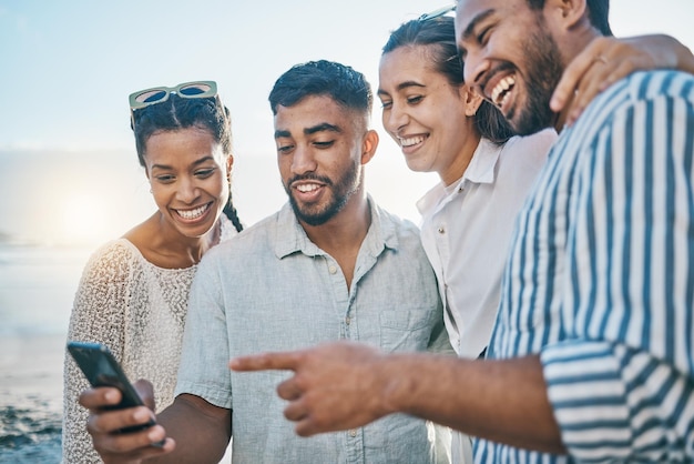 Friends together and phone at ocean with laughing or meme on holiday or weekend to relax Cellphone beach and couple with group are happy on vacation with social media in summer for fun in outdoor