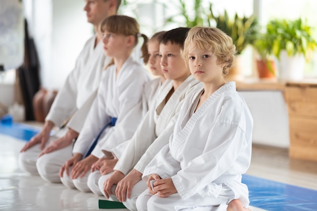 Friends and trainer. Cute blonde-haired boy sitting near friends and trainer before practicing aikido