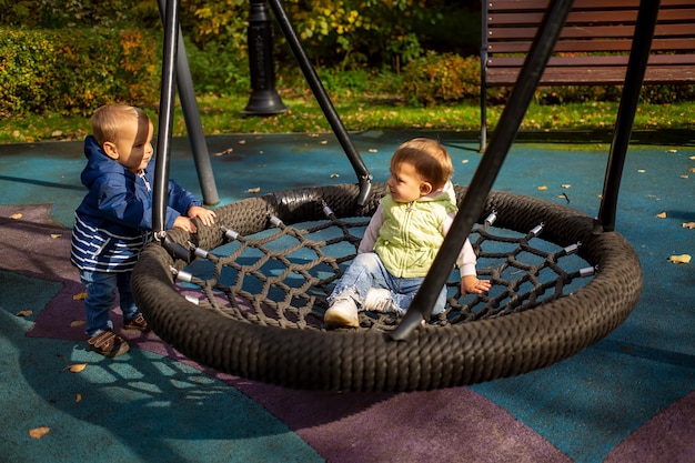 Friends two toddlers boy and girl play and swing on hammock on a playground in autumn park