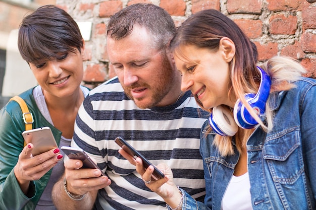 Photo friends using phones against brick wall