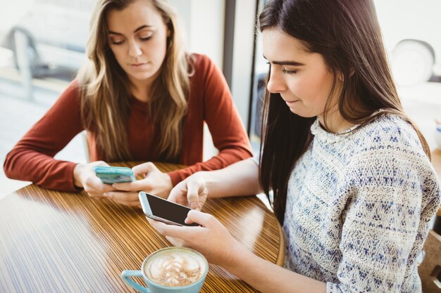 スマートフォンを使用して、コーヒーショップでコーヒーを飲んでいる友人