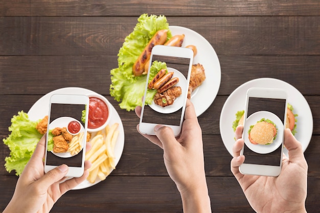 Amici che usano gli smartphone per scattare foto di salsiccia, braciola di maiale, pollo fritto e hamburger