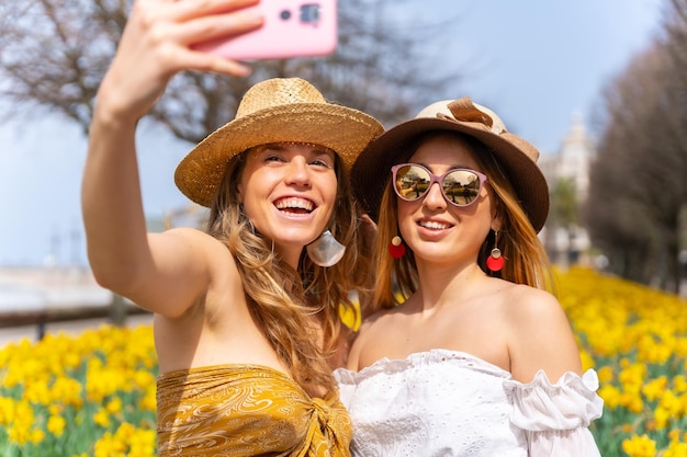 Friends on vacation in the city next to some beautiful yellow flowers taking a selfie with the phone