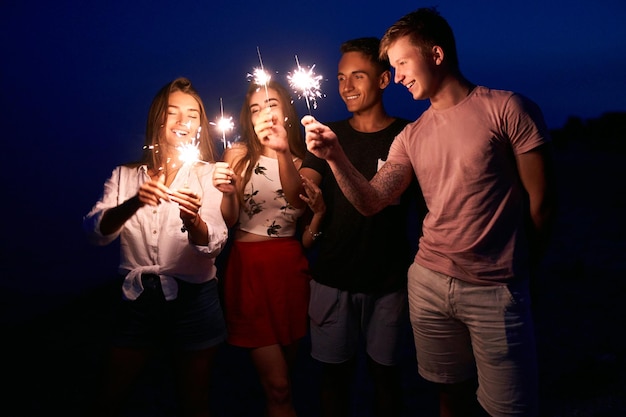 Friends walking dancing and having fun during night party at the seaside with bengal sparkler lights