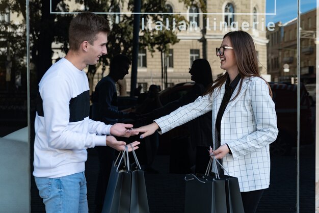 Friends while shopping. Girl and a guy laugh against the background of a store window. Young man and woman with shopping bags.