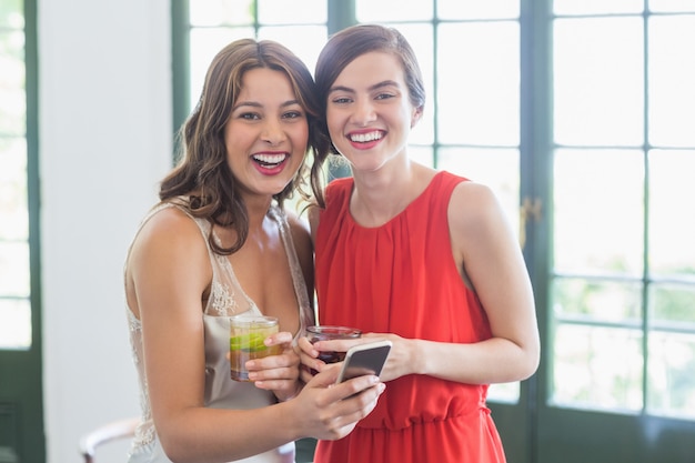 Friends with cocktail glasses laughing while using mobile phone in the restaurant