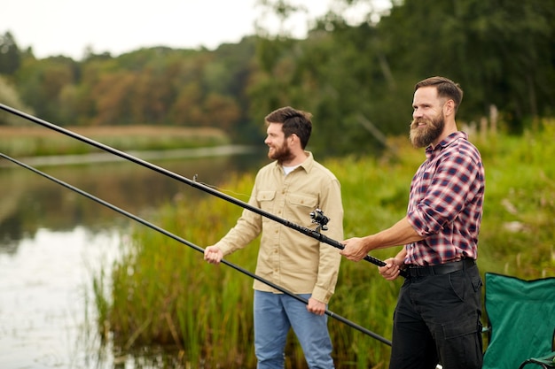 friends with fishing rods at lake or river