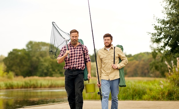 friends with fishing rods and net at lake or river