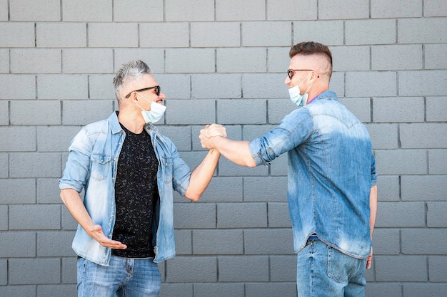 Friends with lowered protective masks doing greetings with handshake during coronavirus outbreak Two friends who no longer respect social distancing New normal concept after coronavirus outbreak