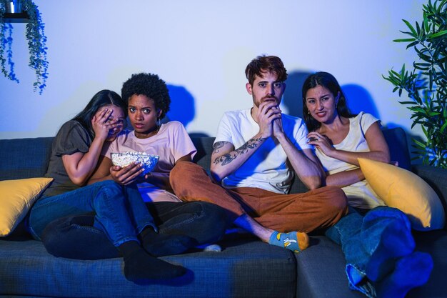 Photo friends with varied ethnic feeling shock while watching a thrilling movie scene expressing fear